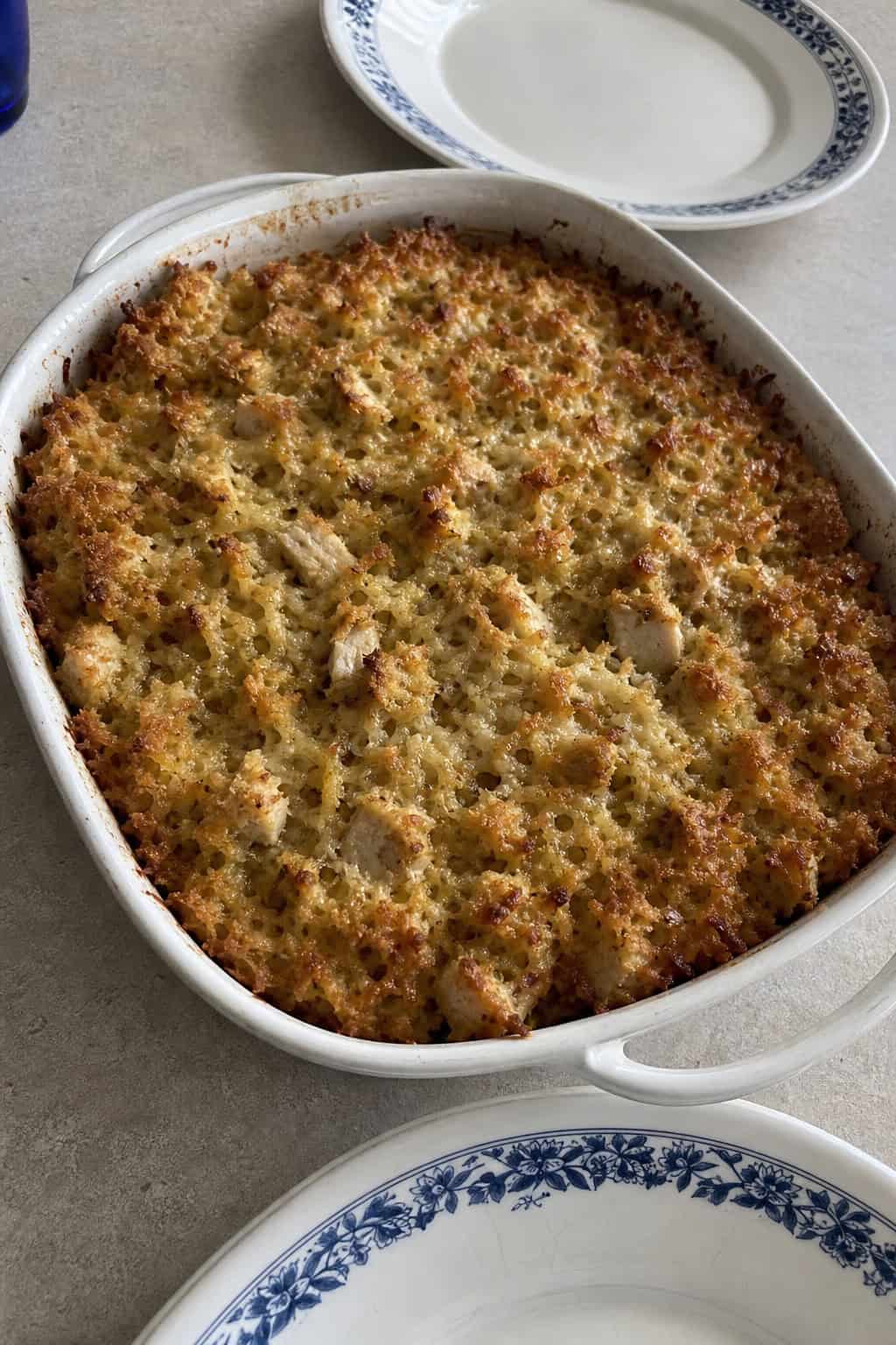 A golden brown hashbrown casserole with turkey and stuffing in a baking dish on a wooden table, garnished with herbs and accompanied by cranberry sauce.