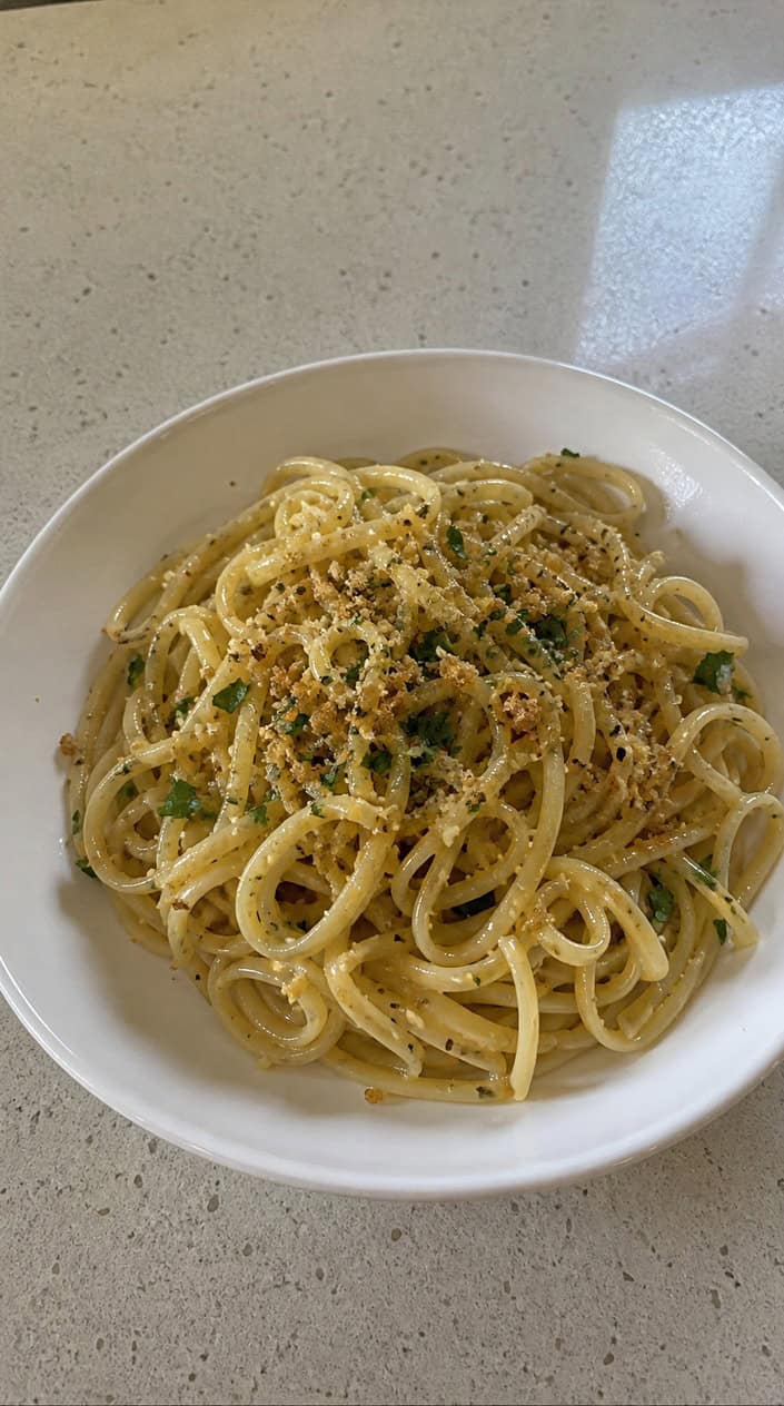A shallow bowl of spaghetti glistening with lemon butter sauce, topped with golden toasted panko breadcrumbs and a scatter of flat-leaf parsley