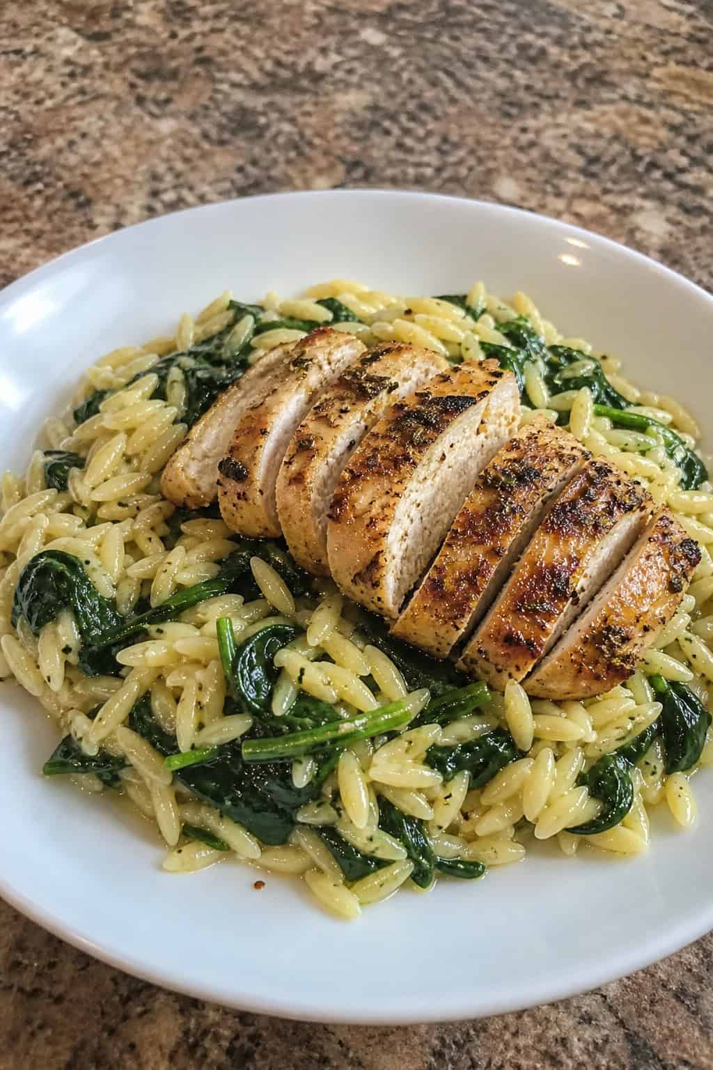 A plate of lemon chicken served over orzo pasta with spinach on a wooden table, garnished with lemon wedges and fresh herbs.