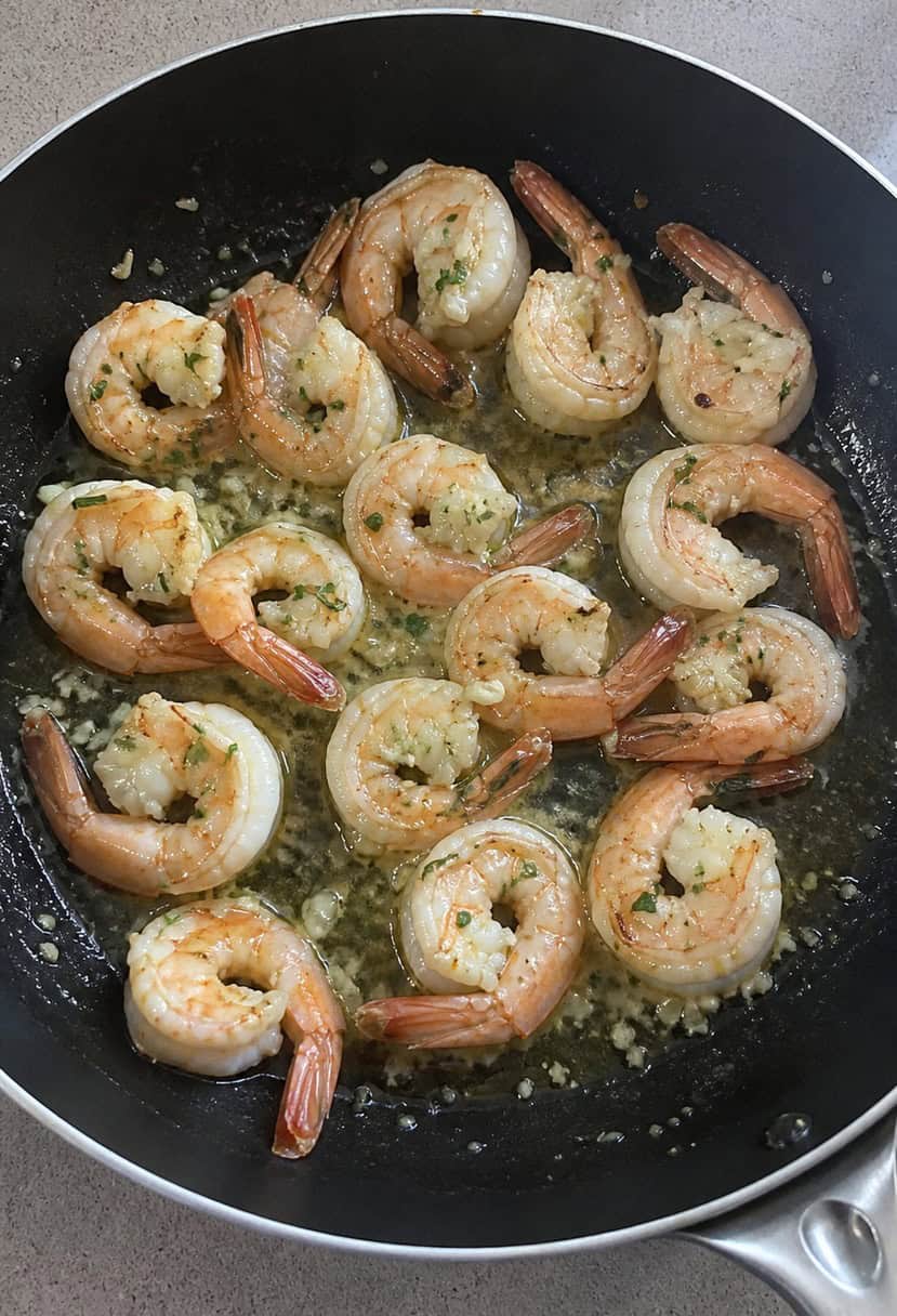 A sizzling skillet of lemon garlic shrimp surrounded by fresh herbs and sliced lemons