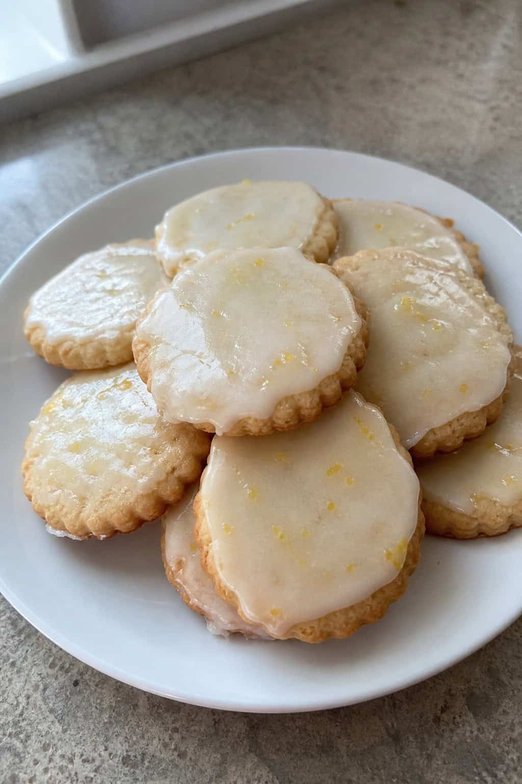 A close-up of lemon-glaze shortbread cookies on a wooden platter with fresh lemon slices and a bowl of lemon glaze nearby.