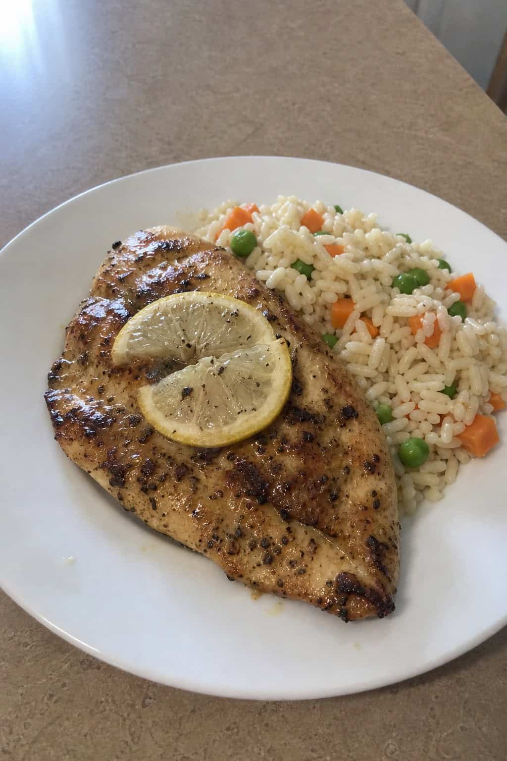 A plate of lemon herb chicken served with rice and garnished with lemon slices and herbs on a wooden table.