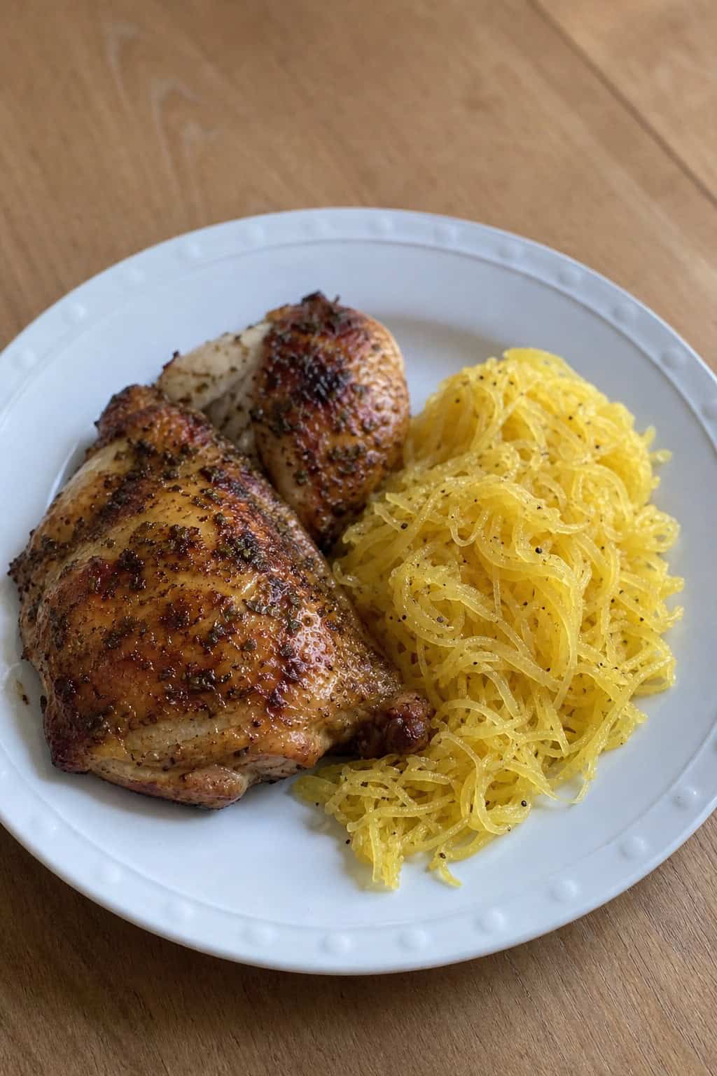 A plate with lemon herb roasted chicken and spaghetti squash garnished with fresh herbs on a wooden table.