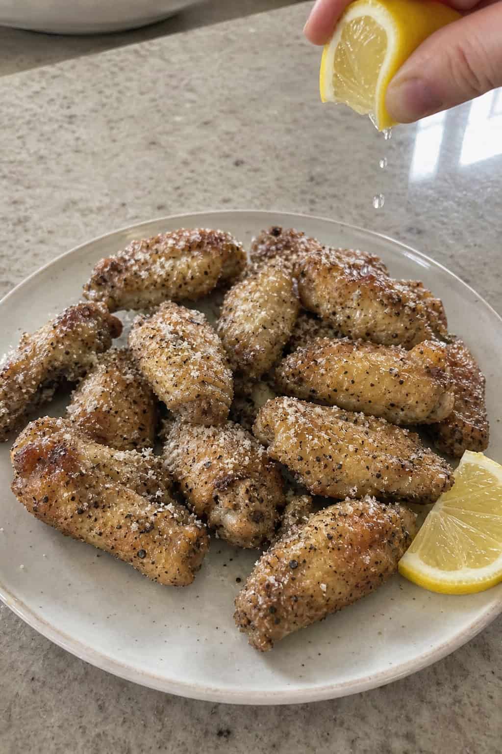 A plate of crispy lemon-pepper parmesan chicken wings with lemon wedges and parsley garnish on a wooden table.