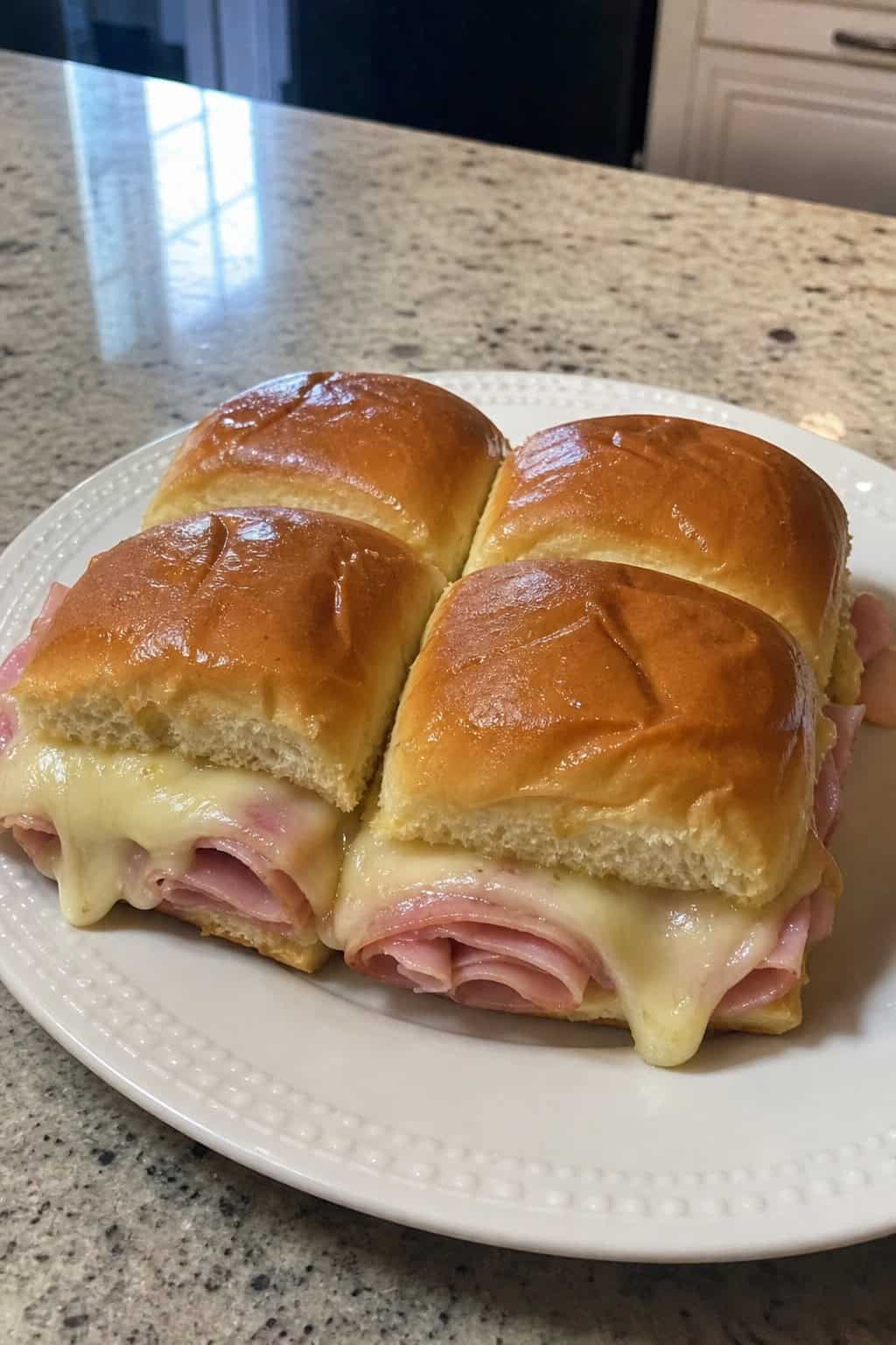 A plate of ham and cheese sliders on Hawaiian rolls with a bowl of honey mustard sauce on the side.