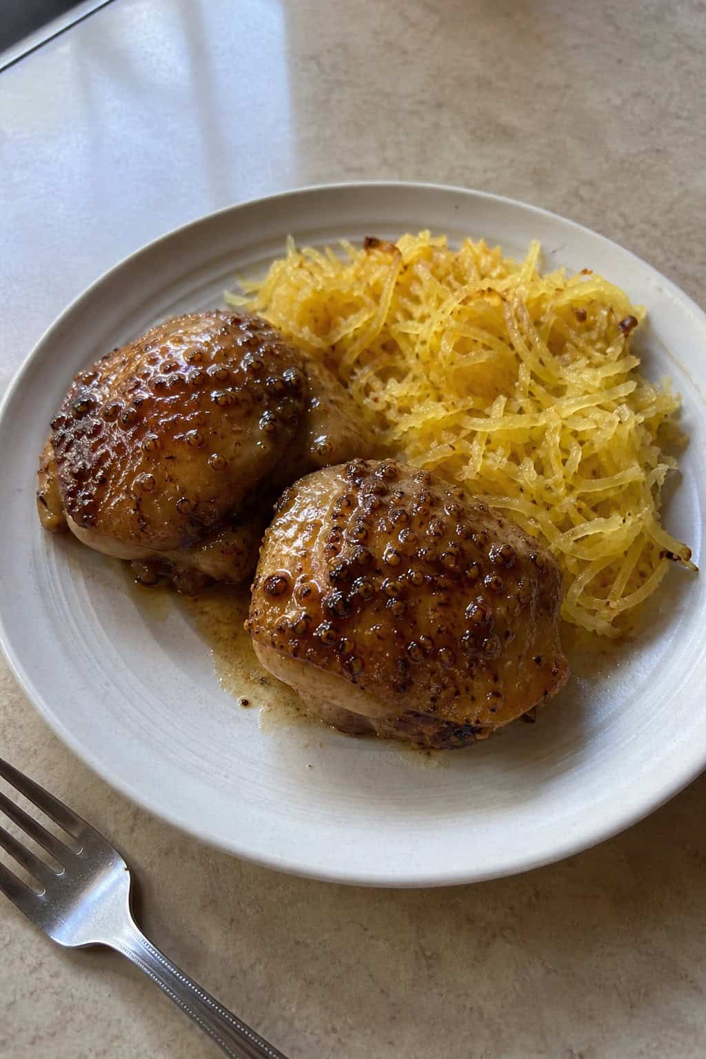 A plate with maple dijon chicken thighs and roasted spaghetti squash garnished with fresh herbs on a wooden table.