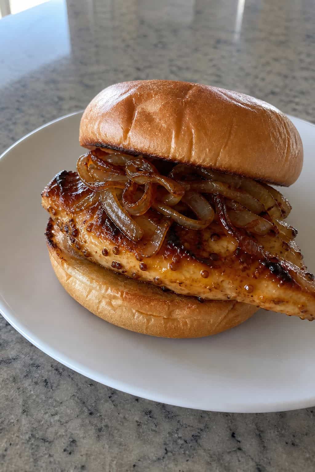 Close-up of a glazed chicken sandwich with sticky maple-Dijon coating and soft caramelized onions on a toasted bun, served on a wooden board
