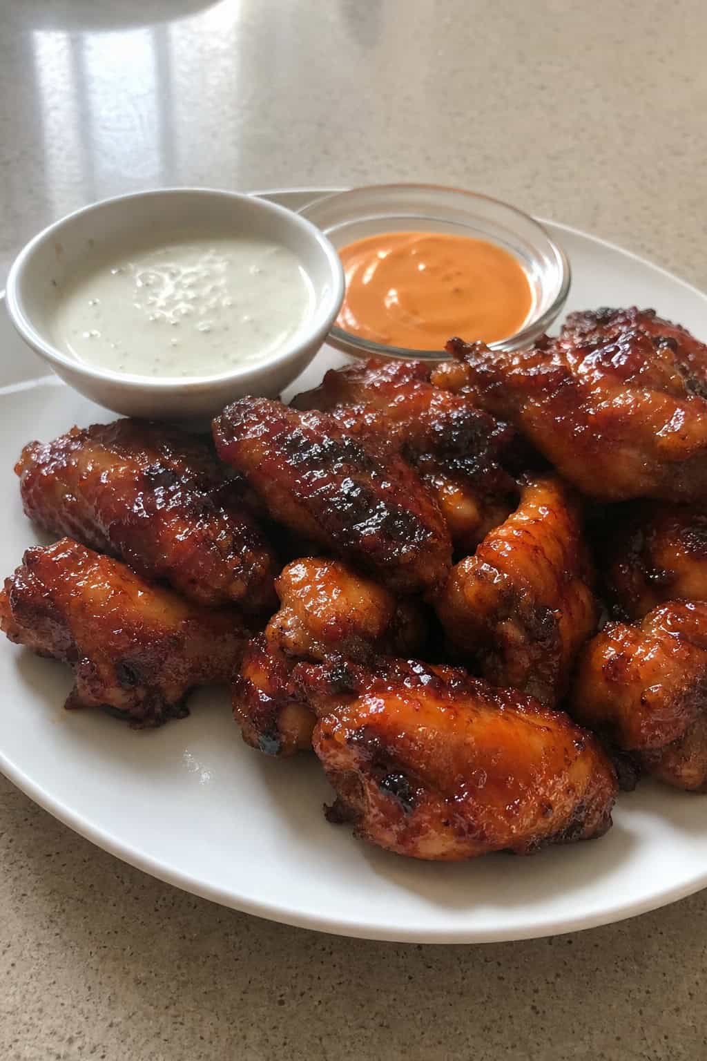 A plate of crispy chicken wings coated in sticky maple-sriracha sauce, garnished with fresh herbs and accompanied by dipping sauces on a wooden platter.