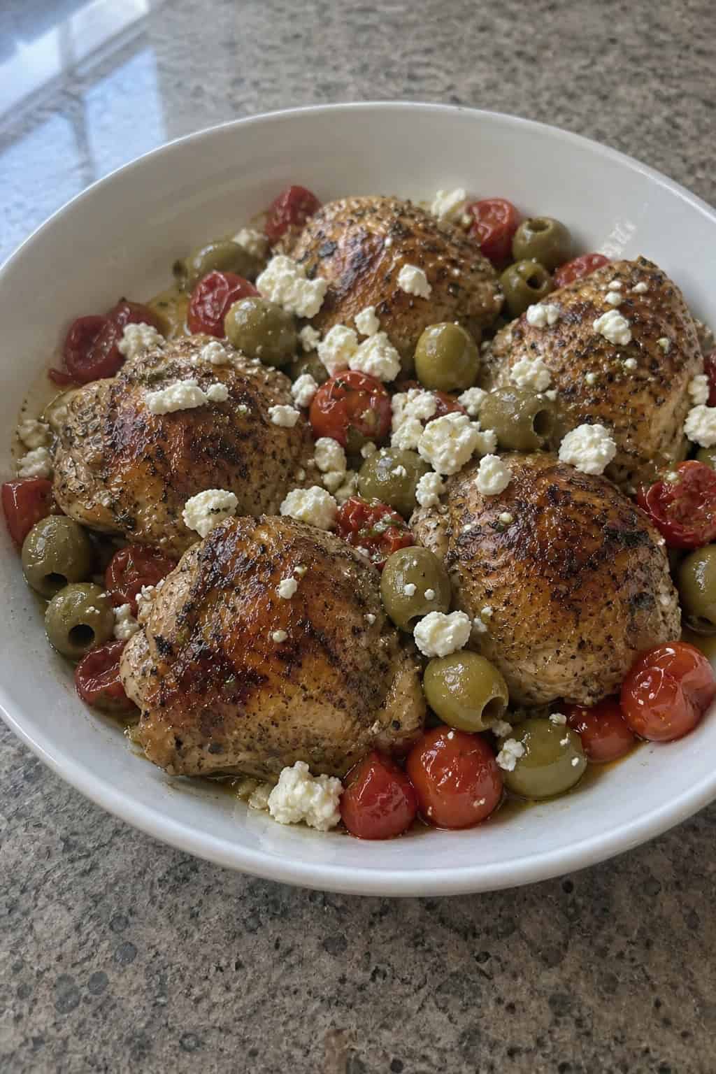 23 Healthy Chicken and Vegetable Recipes 18 A bowl of Mediterranean chicken with olives, tomatoes, and feta cheese garnished with fresh herbs on a wooden table.