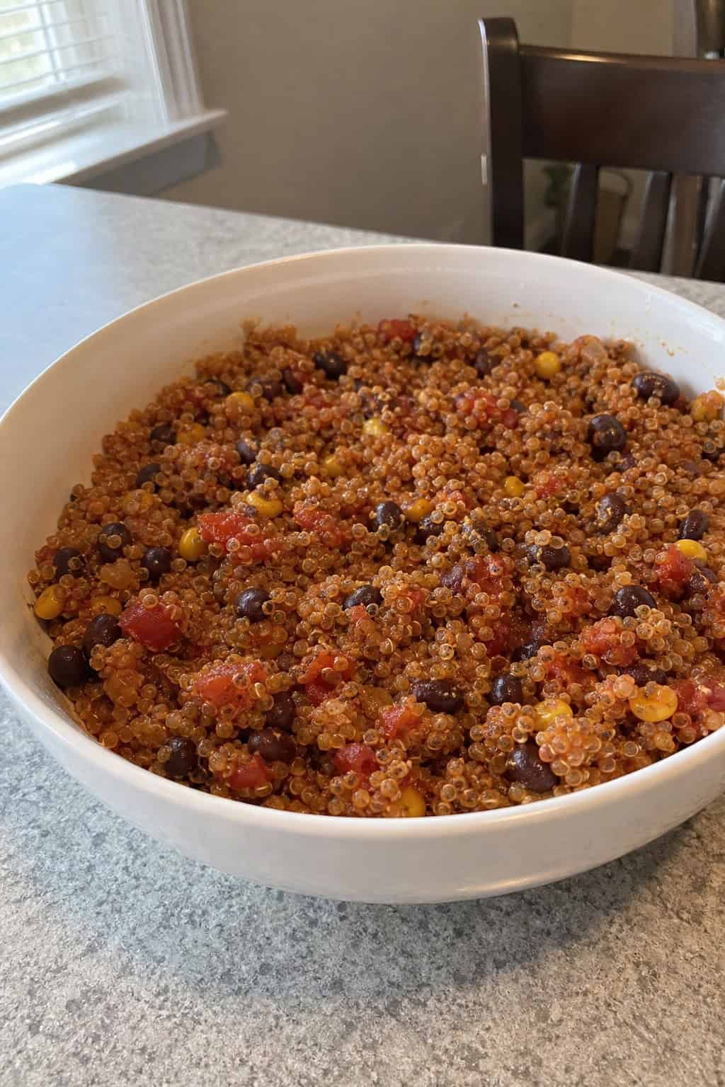 A crockpot filled with Mexican quinoa and black beans surrounded by fresh vegetables on a kitchen countertop.