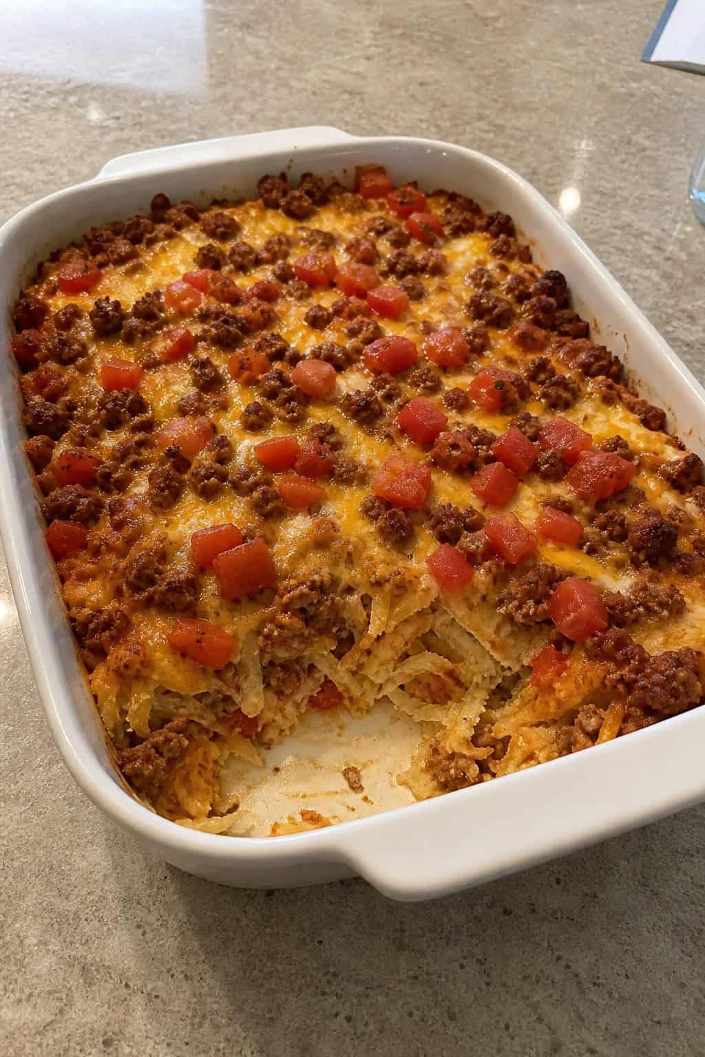 A baked hashbrown casserole with spicy chorizo and melted cheese in a ceramic dish, with a small bowl of salsa and sour cream on the side on a wood table.