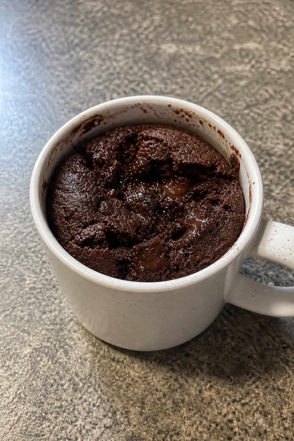 18 Easy Dessert Recipes Ready In Minutes: Quick and Delicious Treats for Any Occasion 3 A ceramic mug filled with a chocolate brownie on a kitchen countertop, with a spoon and chocolate chips nearby.