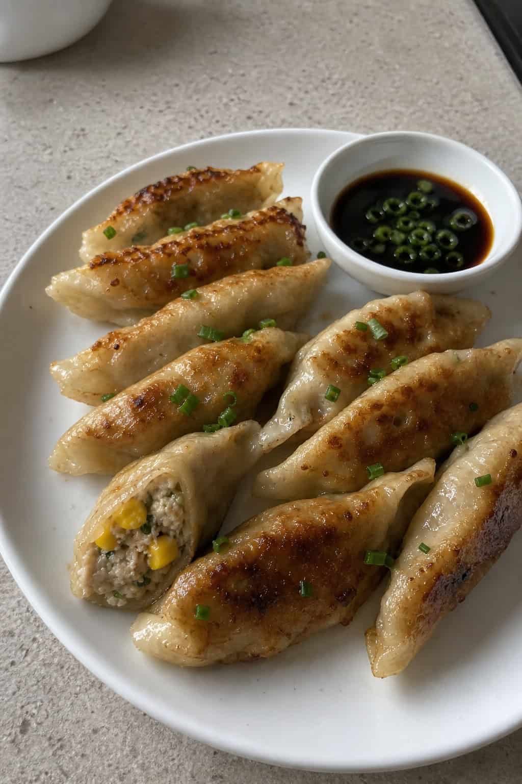 A plate of pan-fried minced chicken and corn gyoza with dipping sauce and green onion garnish on a white plate.
