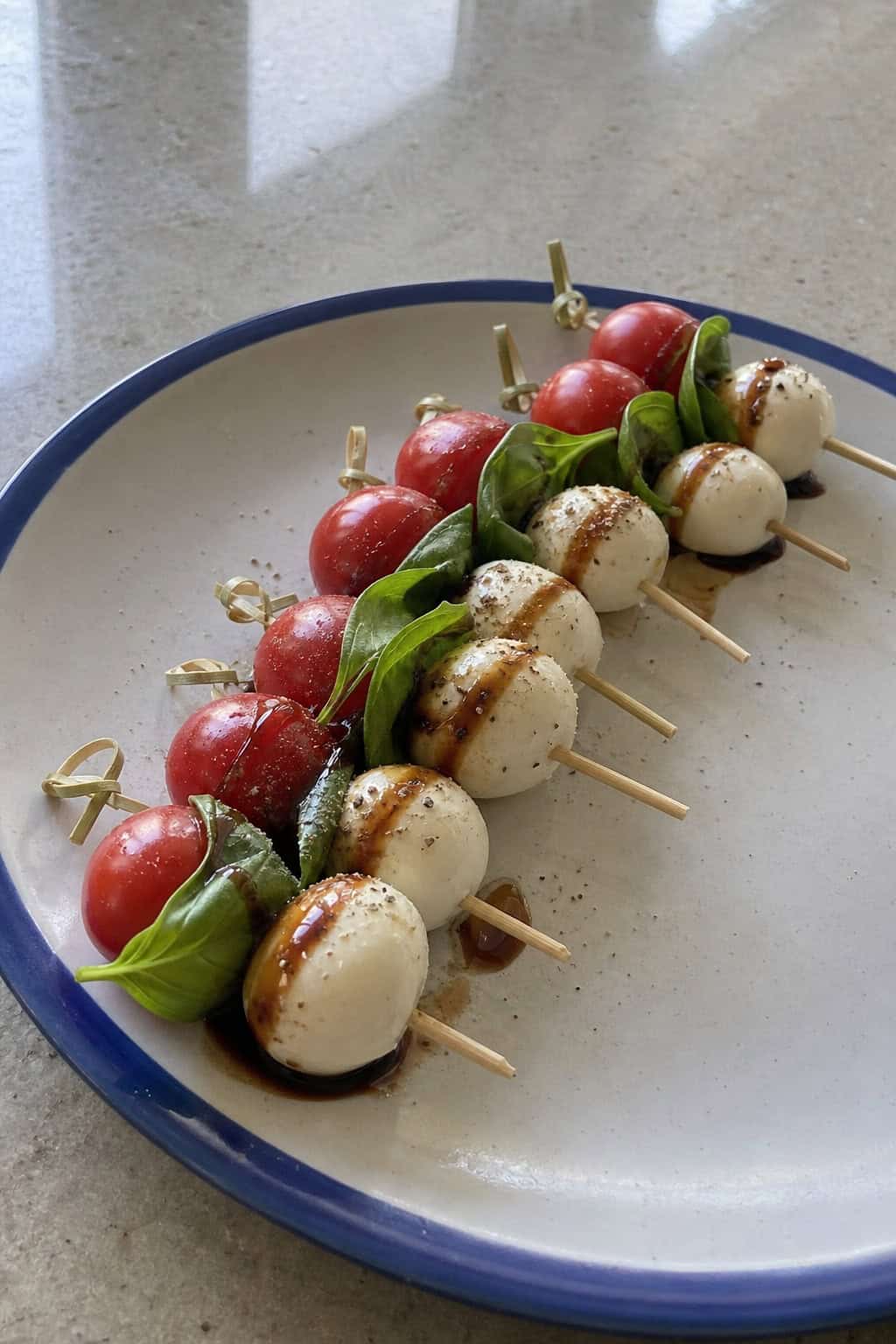 Mini Caprese skewers with cherry tomatoes, basil, and mozzarella on a wooden board with balsamic glaze.