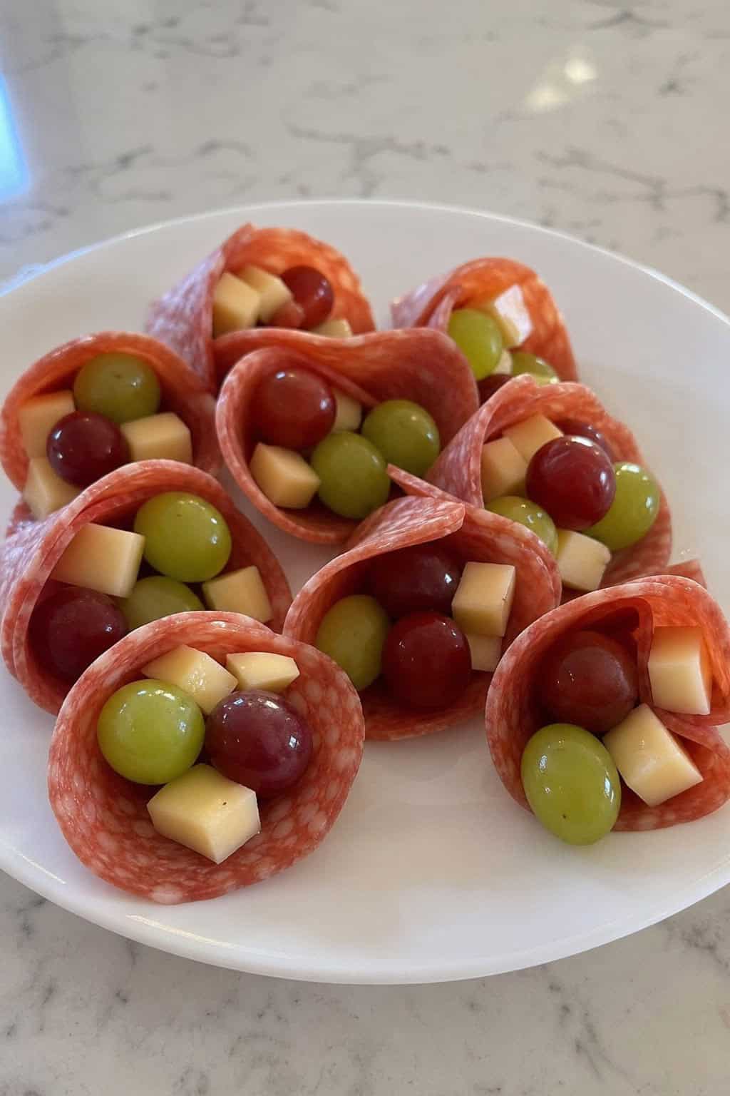 Mini charcuterie cones filled with salami, grapes, and cheese arranged on a wooden serving board.