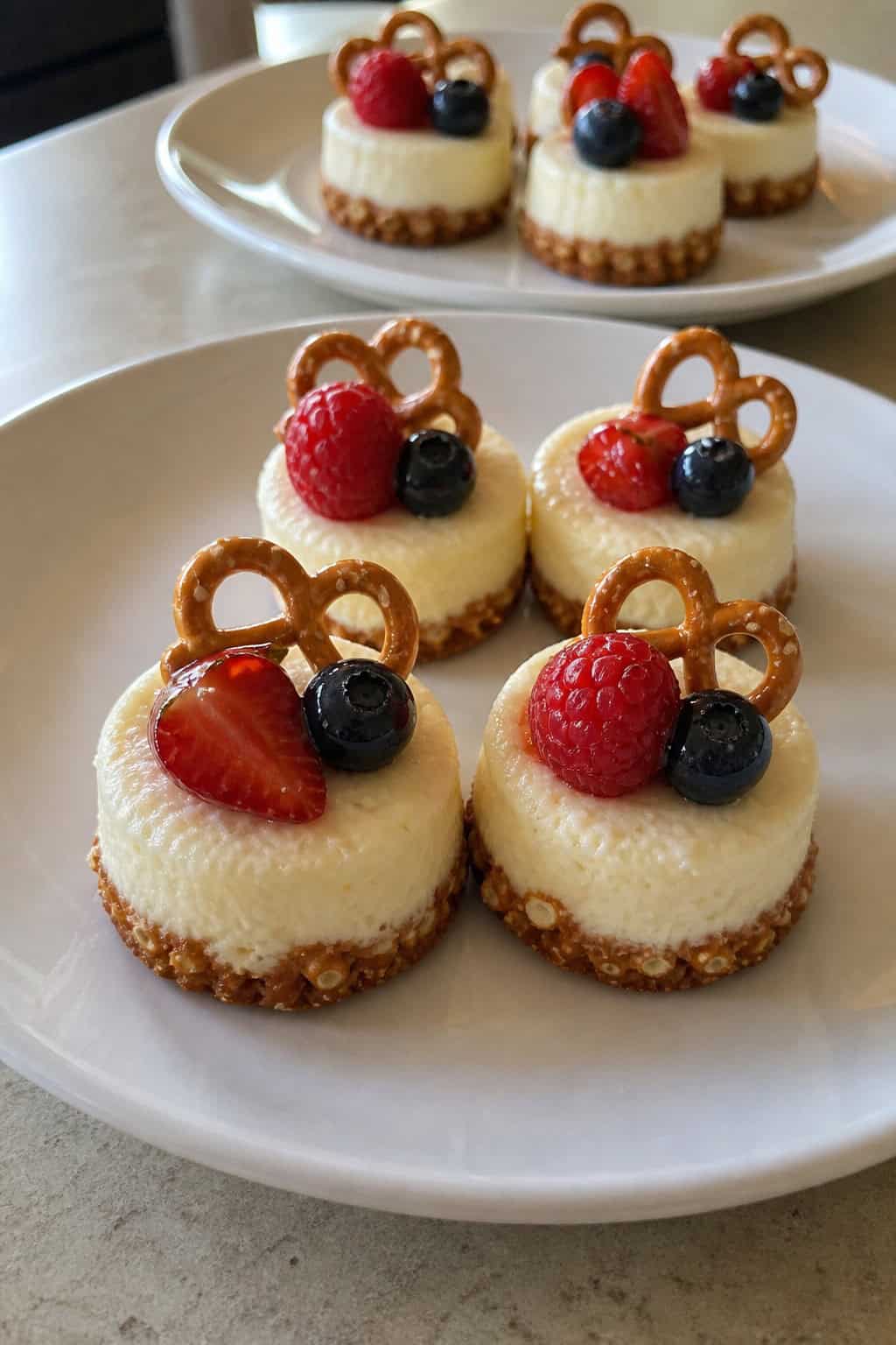 Close-up of bite-sized mini cheesecakes with pretzel crusts arranged on a serving board with scattered pretzel pieces.