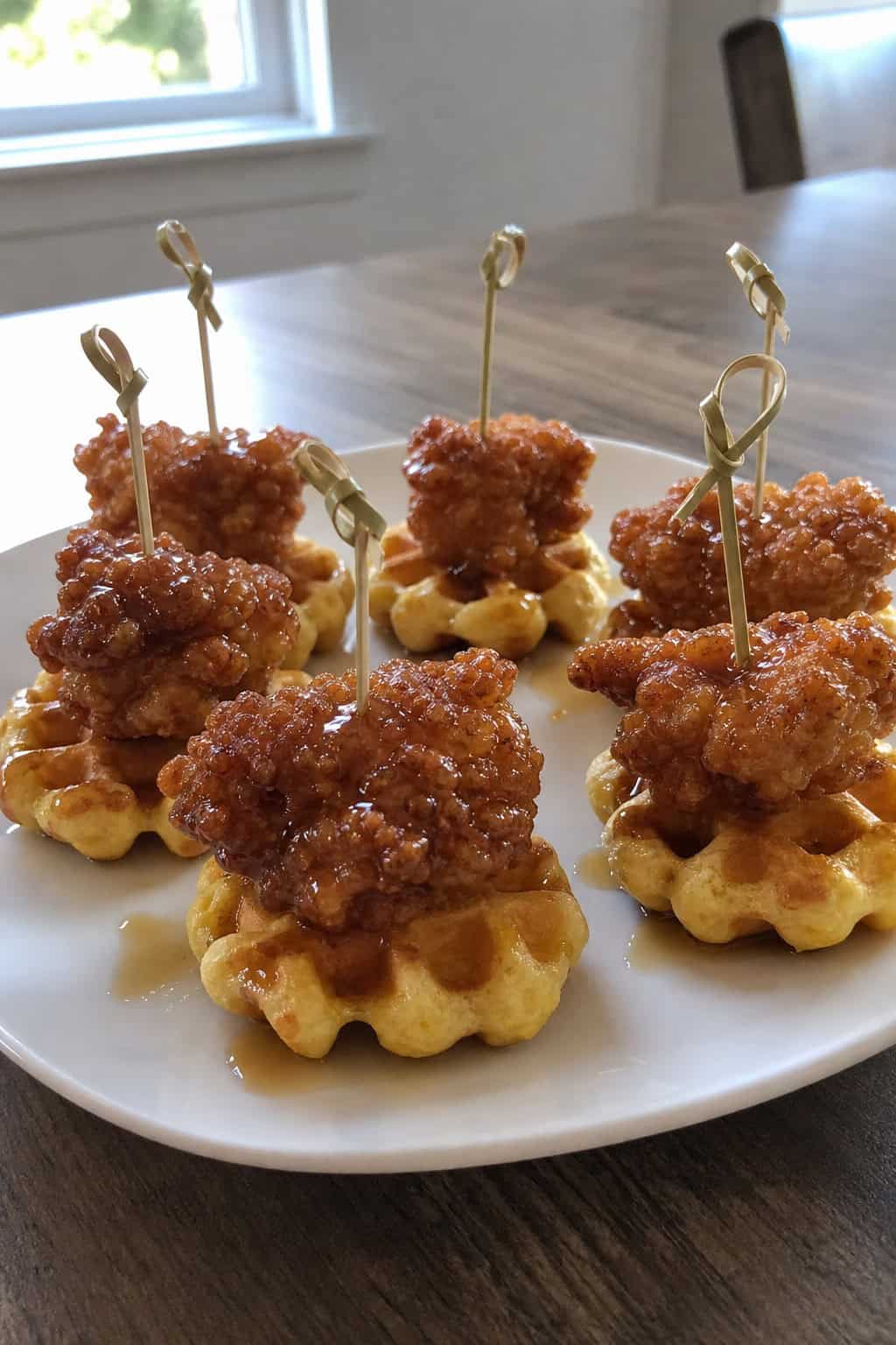 Close-up of mini chicken and waffle bites arranged on a wooden serving board with syrup drizzled on top.
