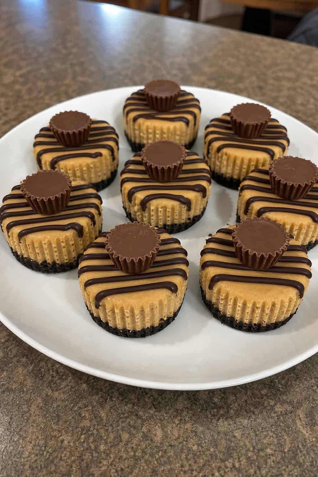 A platter of mini peanut butter cup cheesecakes topped with chocolate and peanut butter cups on a wooden table with party decorations.