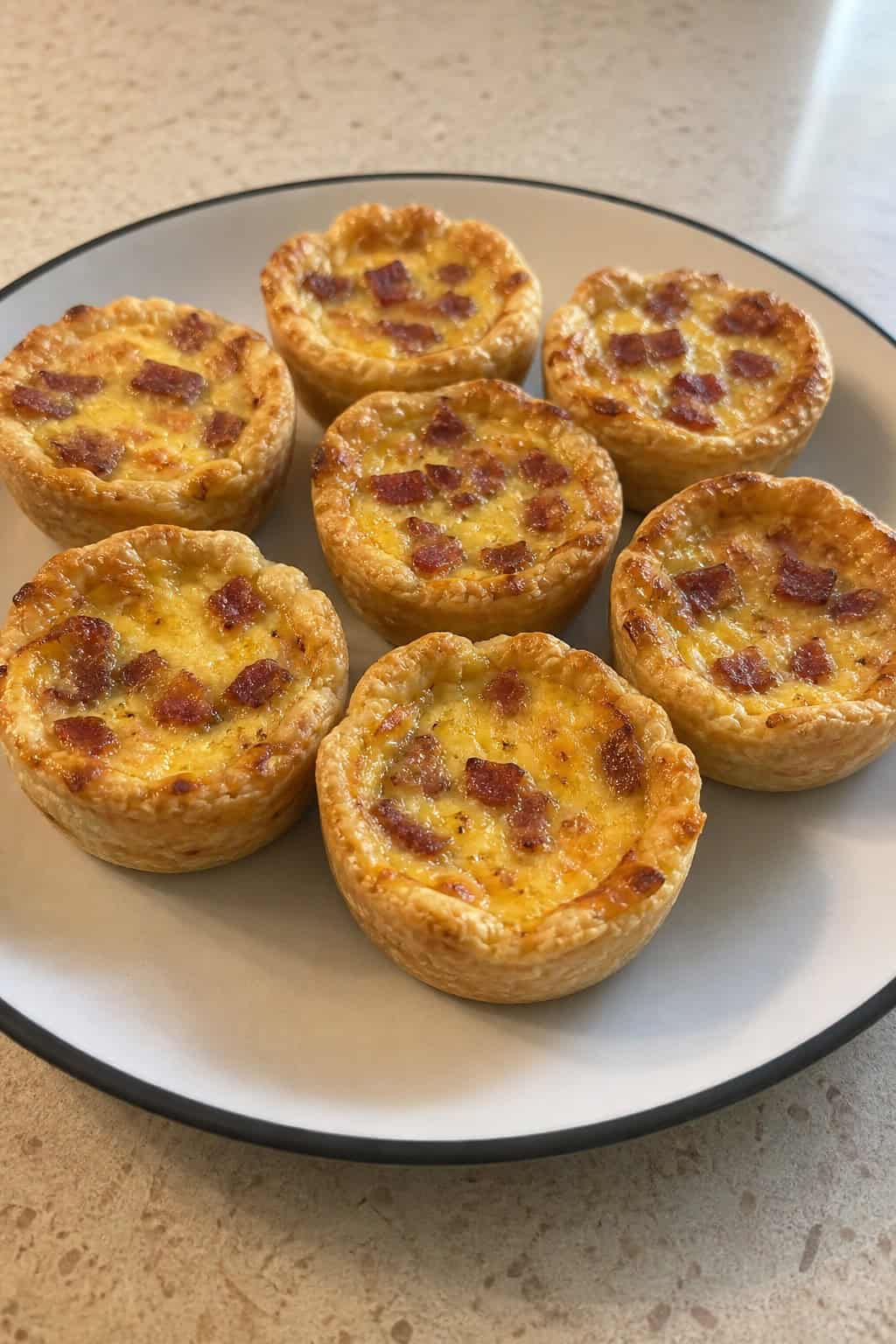 Close-up of mini Quiche Lorraine on a wooden board with fresh ingredients around, ready to serve.
