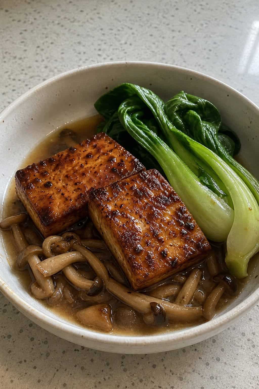 A bowl of miso-glazed tofu with bok choy and mushroom stems in broth.