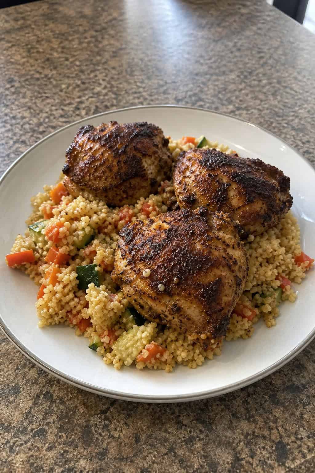 25 Chicken Thigh Recipes for Easy Weeknight Dinners 10 A plate of Moroccan-spiced chicken thighs served with couscous and garnished with fresh herbs on a wooden table.