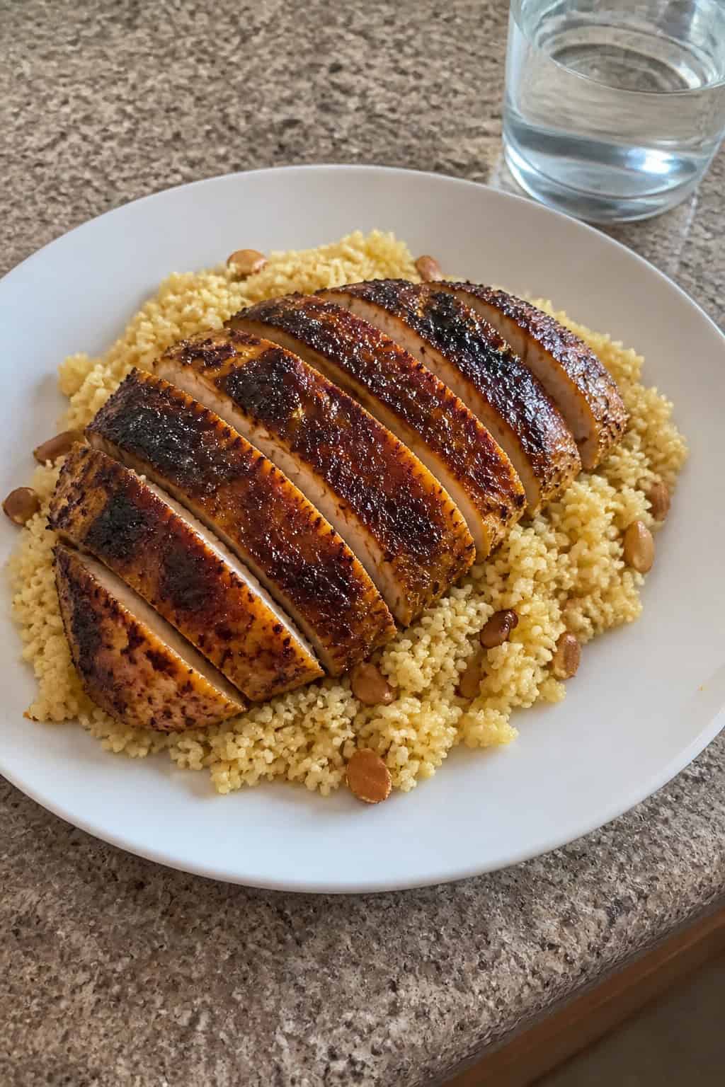 29 Mouthwatering Chicken Breast Recipes to Spice Up Your Dinner Routine! 18 A plate of Moroccan-spiced chicken breast served on a bed of couscous garnished with parsley and almonds on a wooden table.