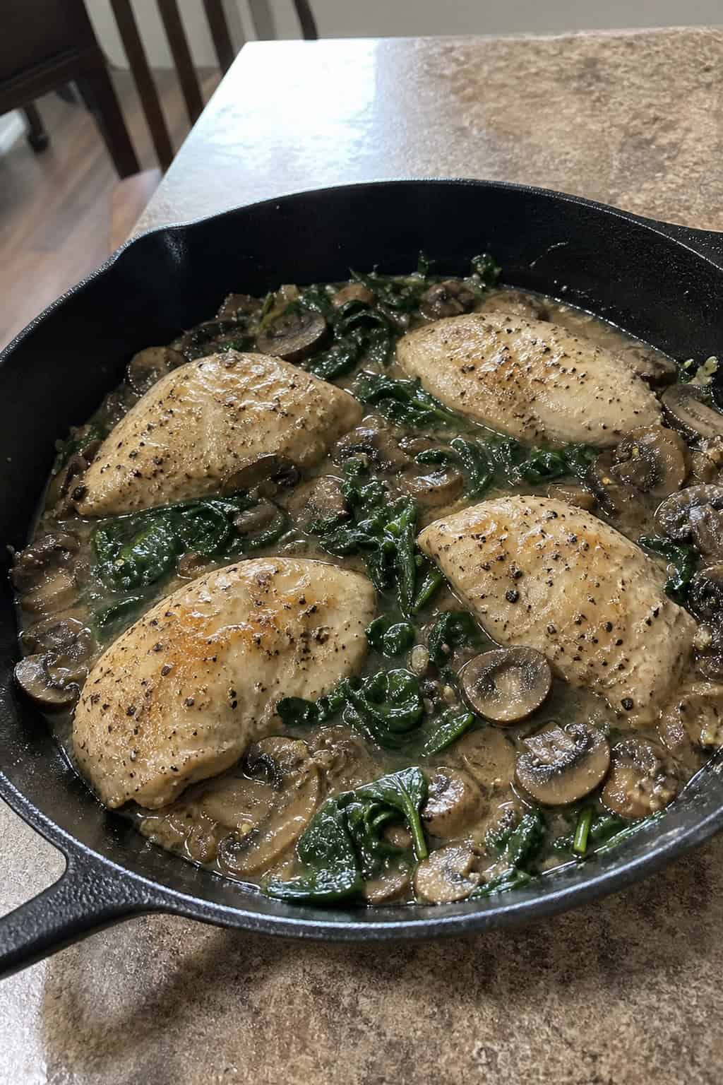 25 Heart-Healthy Chicken Recipes to Keep You Feeling Great! 16 A skillet with cooked chicken breasts, mushrooms, and spinach on a wooden table surrounded by fresh ingredients.