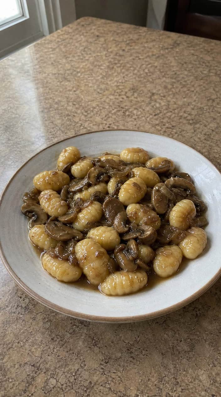Deeply browned cremini mushrooms and pillow-soft gnocchi in a mahogany-toned Marsala sauce, topped with chopped flat-leaf parsley and a dusting of Parmesan, served in a wide shallow bowl.