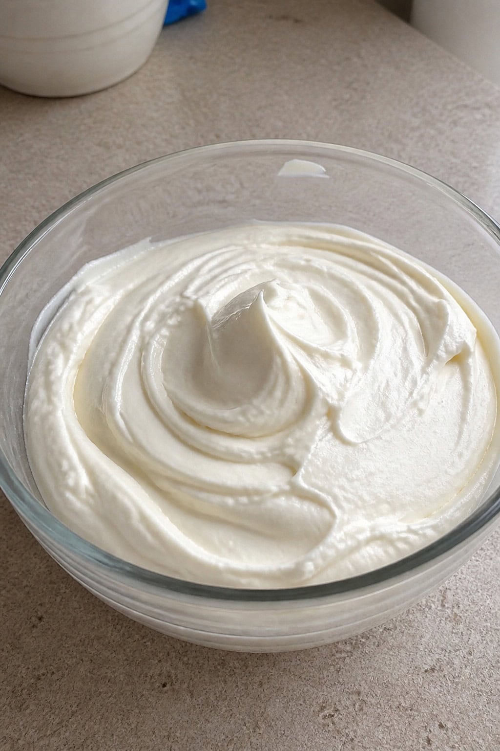 A bowl of creamy no-bake Philadelphia whipped cheesecake filling surrounded by baking ingredients on a kitchen countertop.