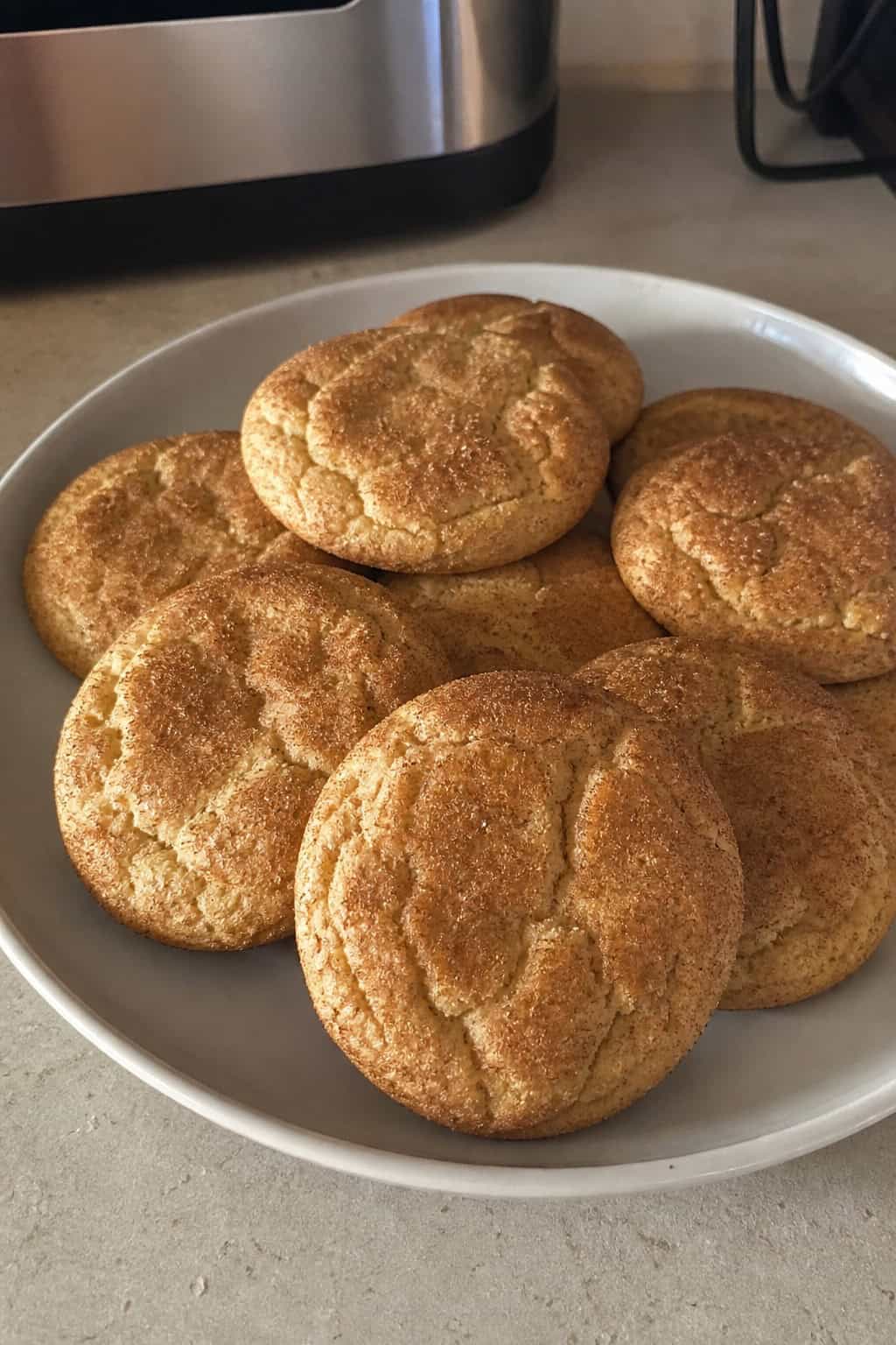 A close-up of freshly baked banana snickerdoodle cookies on a wooden board with ripe bananas and cinnamon nearby.