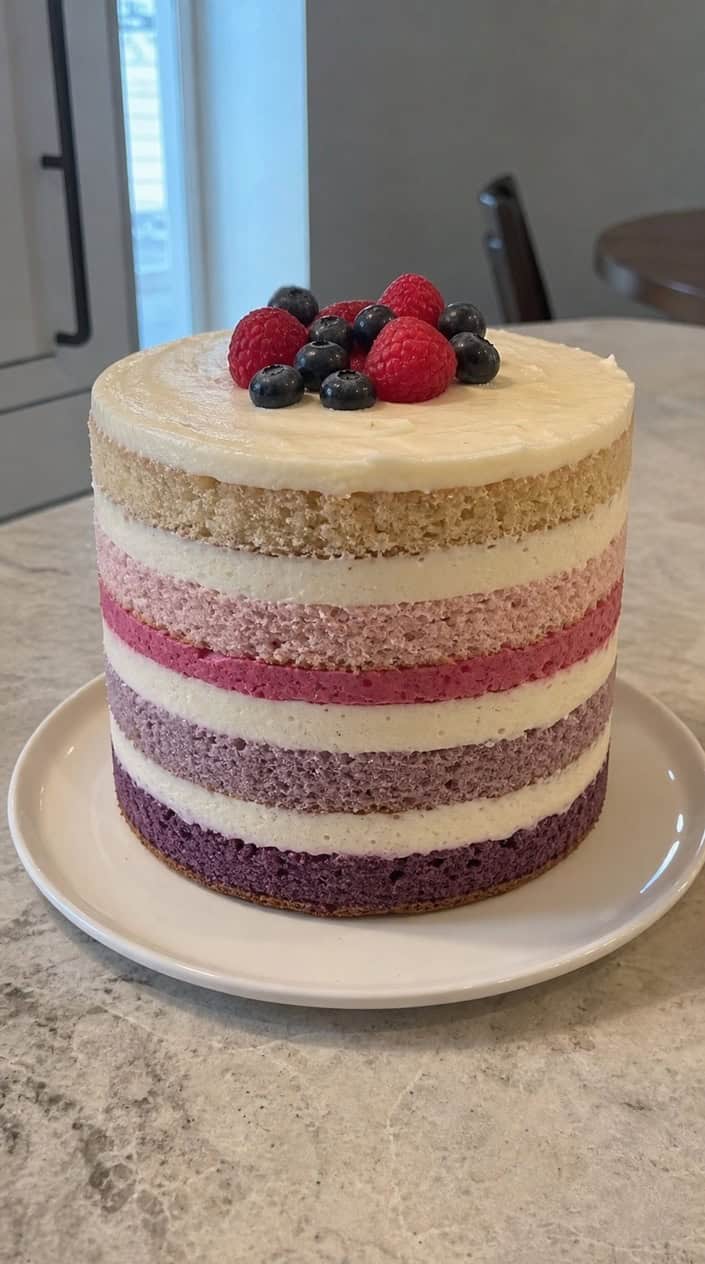 A multi-layered ombre naked cake with a brightly colored buttercream center on a white cake stand.