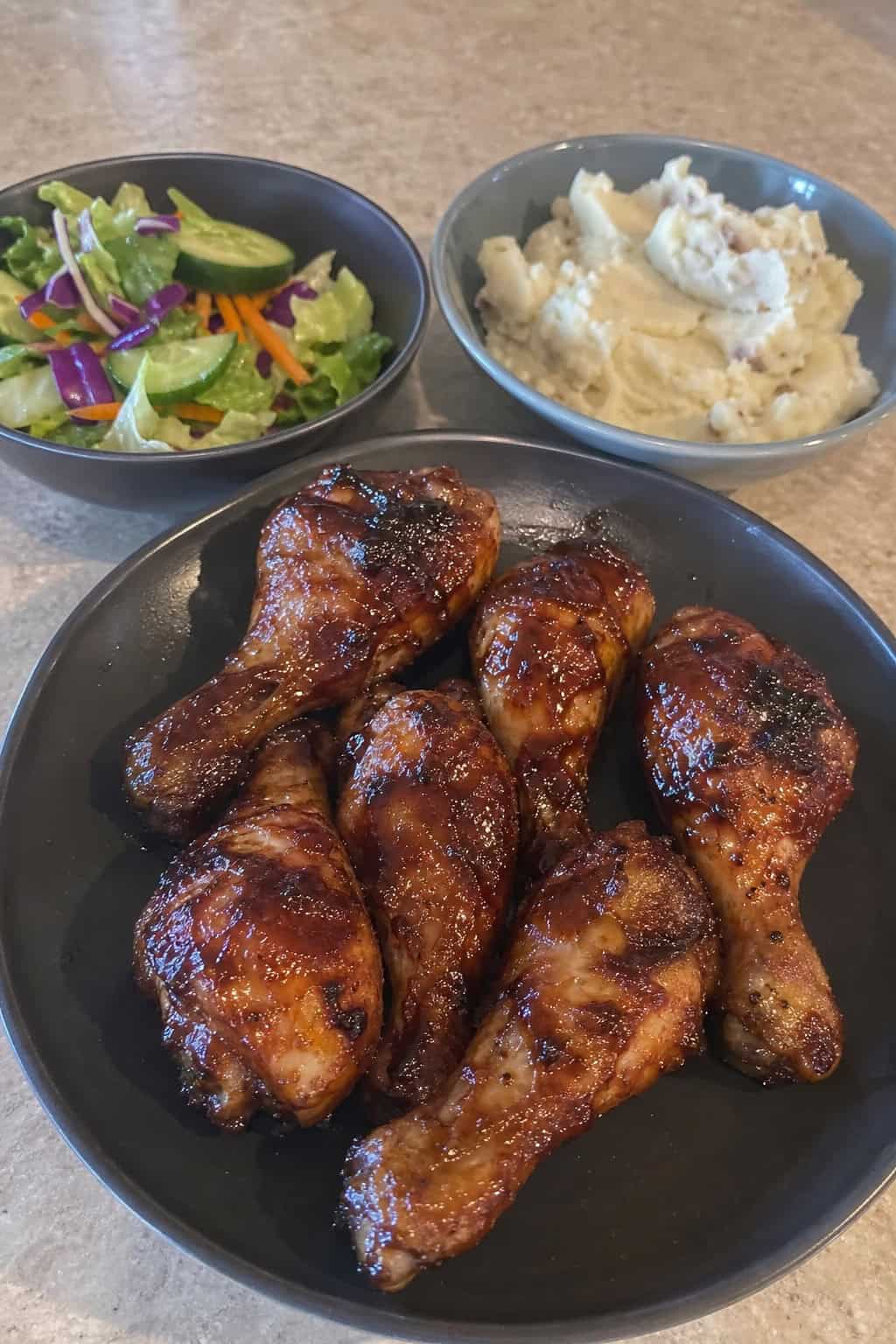 BBQ ranch chicken legs in a cast iron skillet with caramelized skin and fresh herb garnish, surrounded by roasted potato wedges on a wooden table.