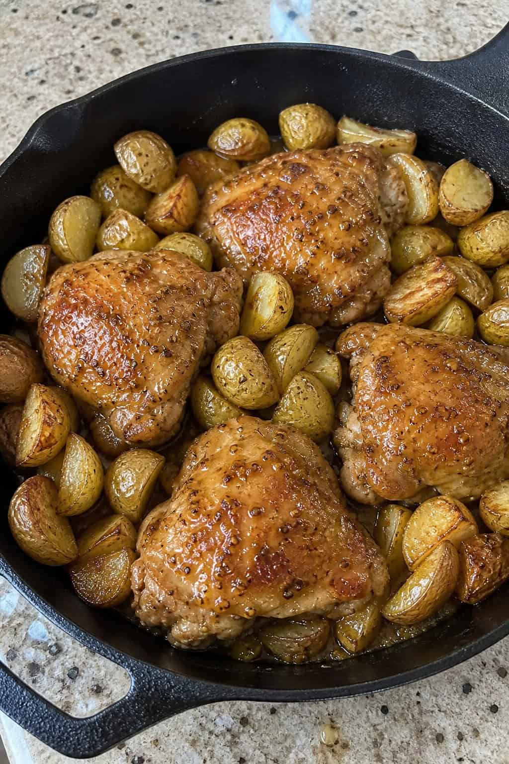 25 Chicken Thigh Recipes for Easy Weeknight Dinners 3 A skillet with honey mustard glazed chicken thighs and roasted potatoes garnished with herbs on a wooden table.