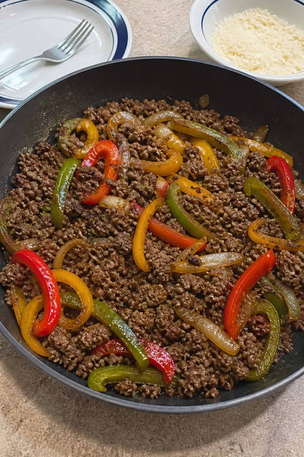 18 Easy Ground Beef Recipes for Weeknight Dinners 2 A skillet filled with cooked ground beef, colorful bell peppers, and onions on a wooden table, garnished with fresh herbs.