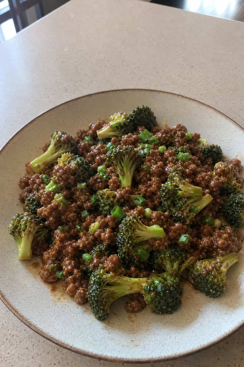 A skillet filled with cooked ground beef and broccoli coated in hoisin sauce on a wooden table.