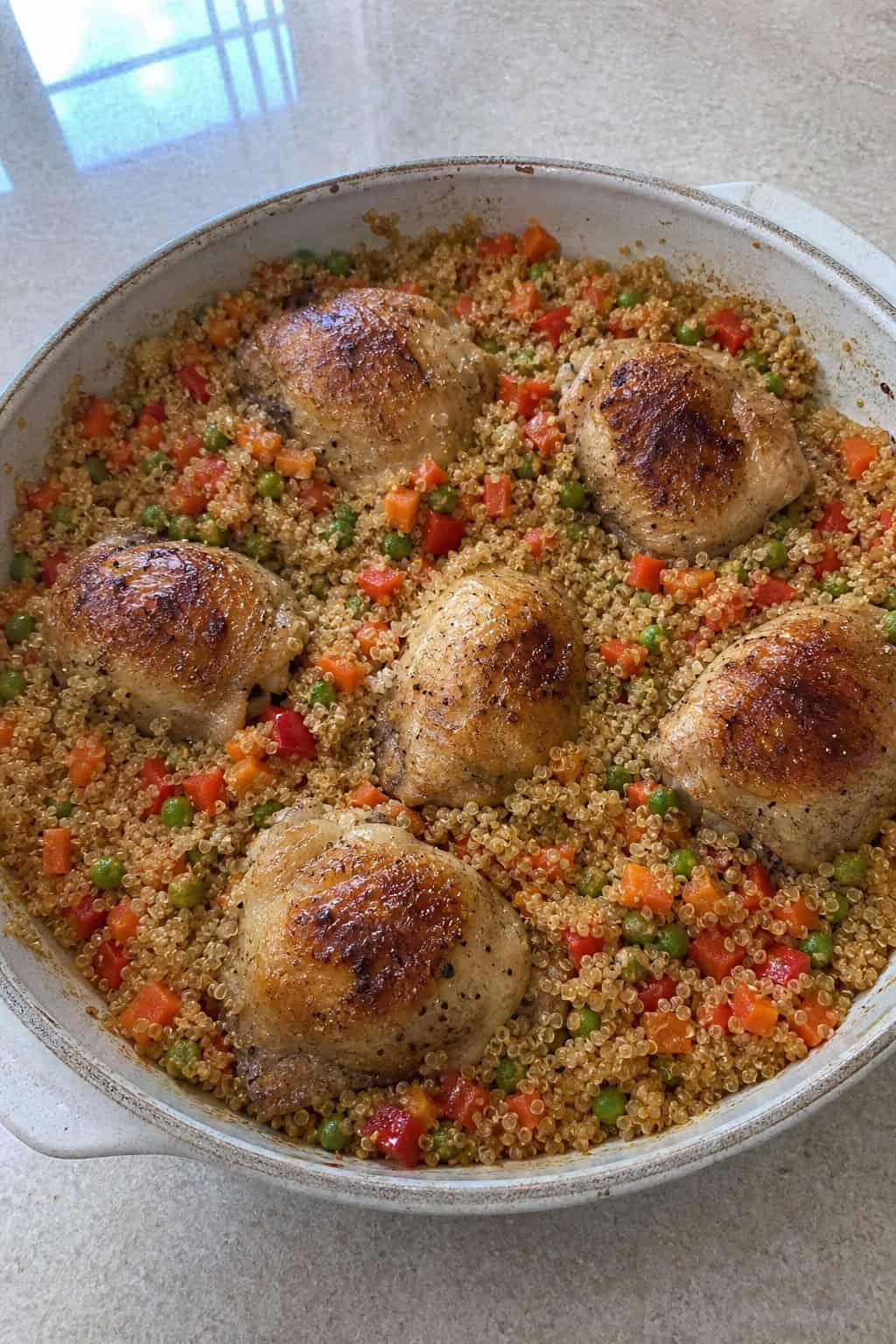 A ceramic dish of cooked chicken and quinoa casserole with vegetables on a kitchen countertop.