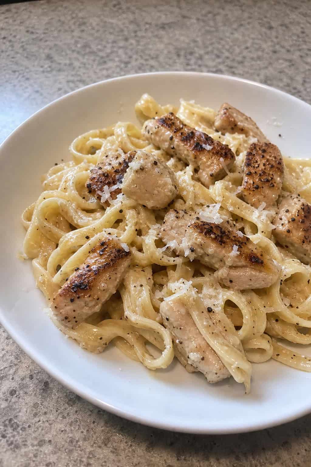 A bowl of creamy garlic parmesan chicken pasta garnished with parsley and parmesan cheese on a wooden table.