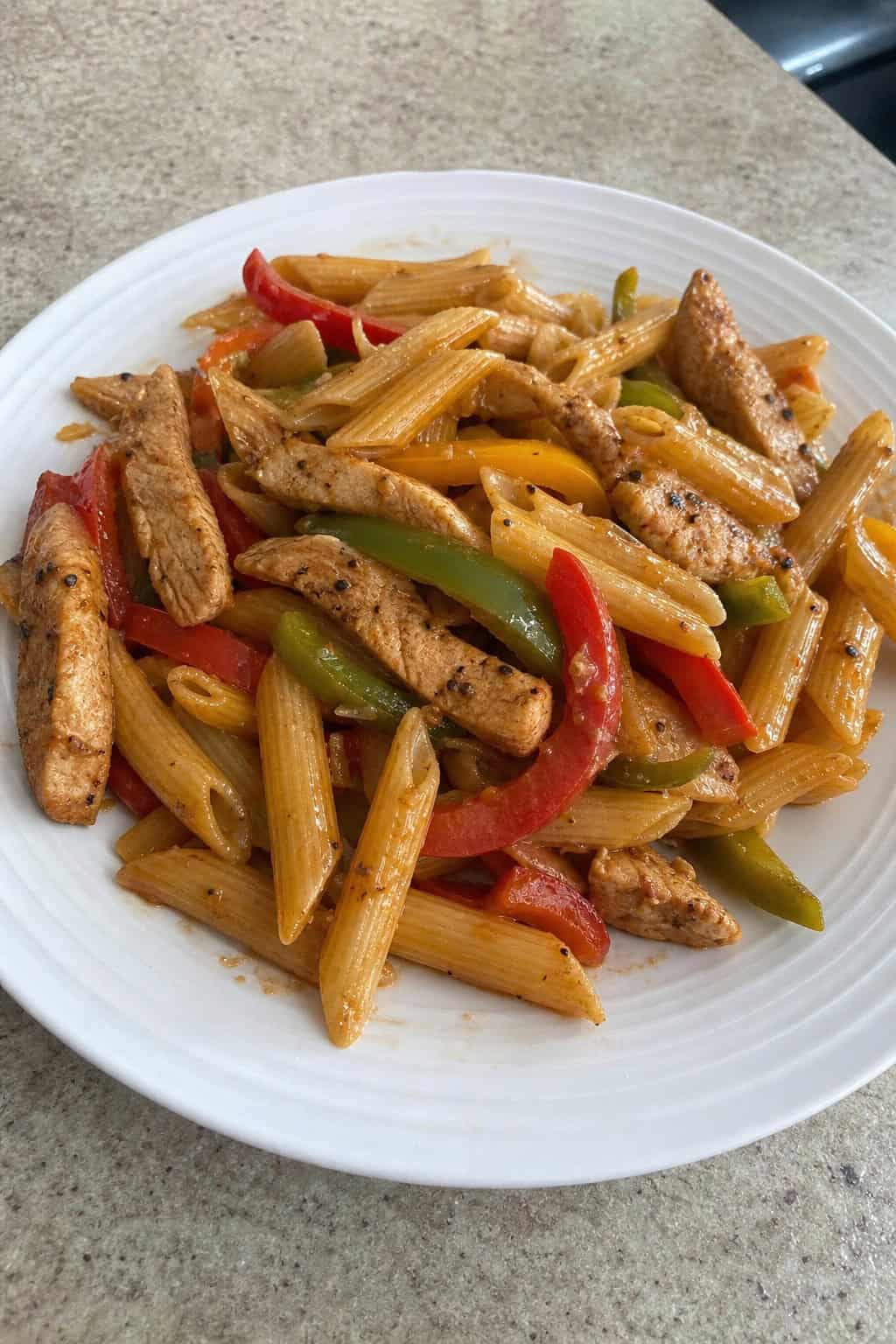 A skillet filled with chicken fajita pasta, colorful bell peppers, onions, and garnished with fresh cilantro on a wooden table.