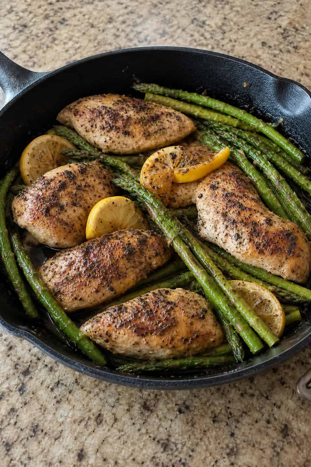 23 Healthy Chicken and Vegetable Recipes 19 A skillet with lemon herb chicken and green asparagus on a wooden table.