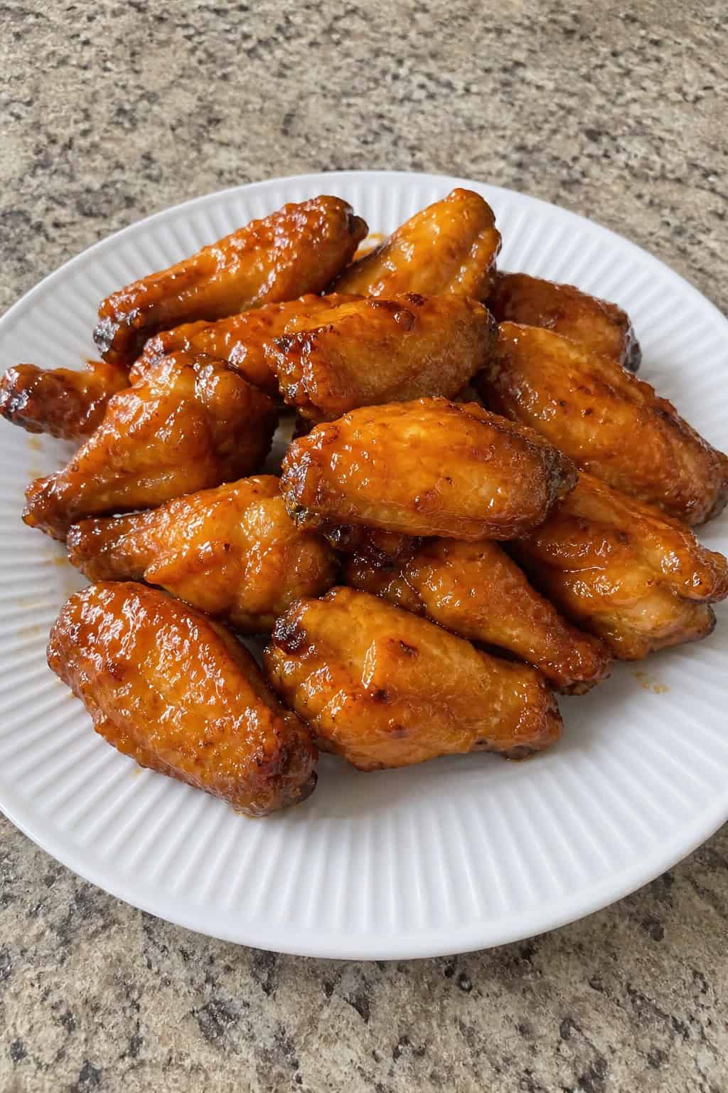22 Chicken Wing Recipes for Game Day and Beyond 16 A plate of orange-miso glazed chicken wings garnished with ginger slices and green onions on a wooden table.