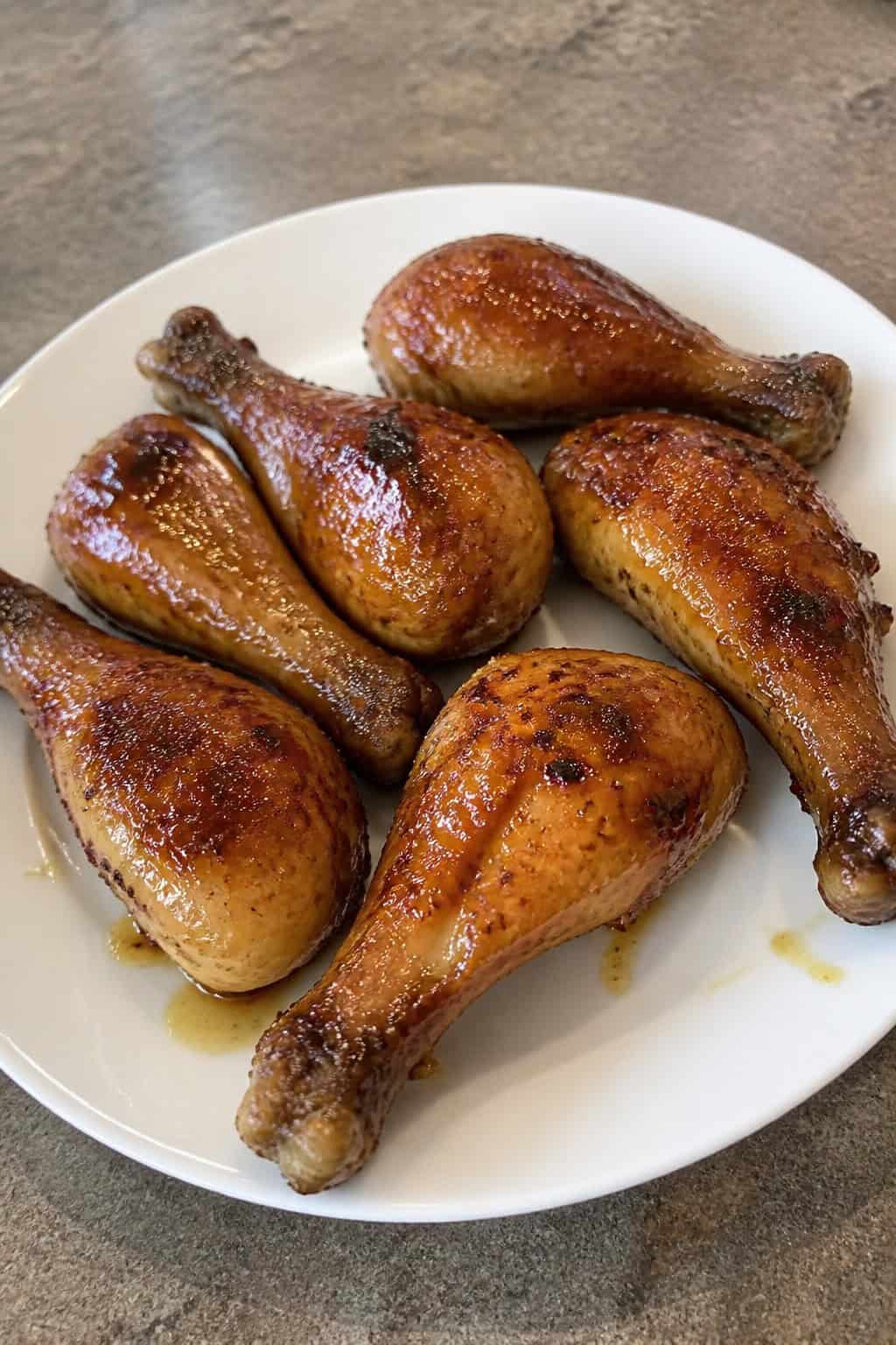 Oven-baked chicken legs on a wooden platter with a deep amber honey-garlic glaze, scattered fresh parsley, and small bowls of honey and minced garlic nearby.
