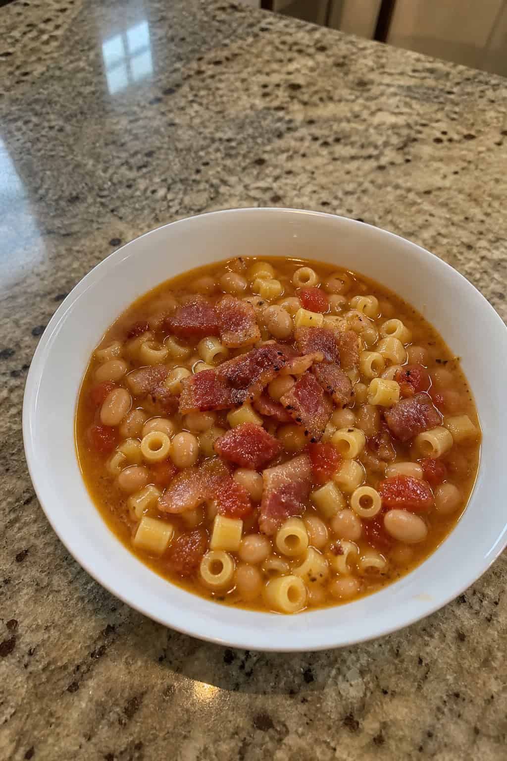 31 Cozy Healthy Soup Recipes for Winter 21 A bowl of Pasta e Fagioli soup with pasta, white beans, and pancetta garnished with herbs on a wooden table surrounded by ingredients.