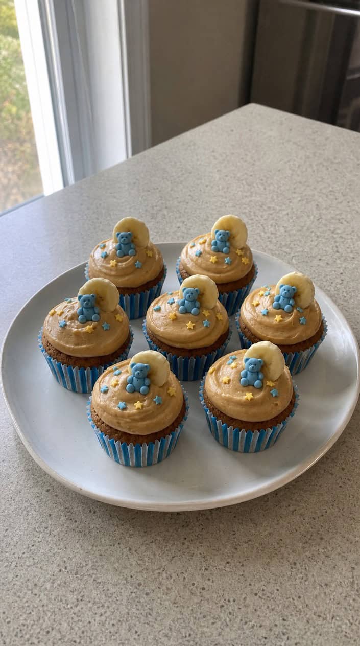 A plate of peanut butter banana smash cupcakes with baby-themed decorations in the background.