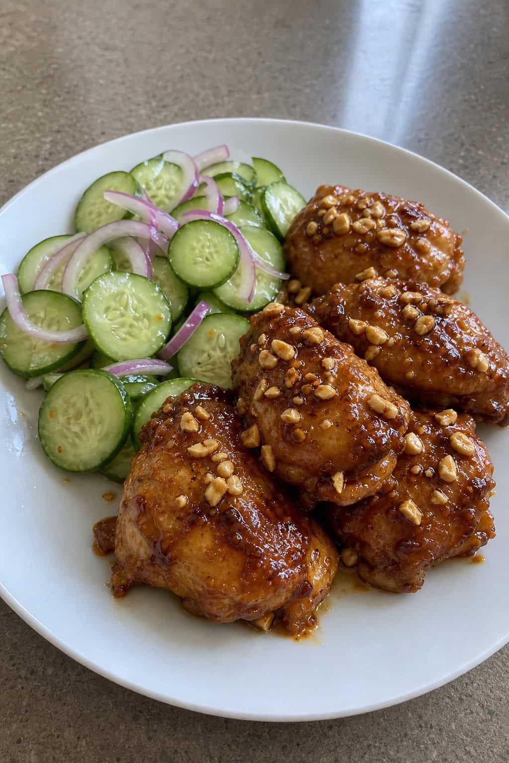 A plate of peanut satay chicken thighs served with a fresh cucumber salad.