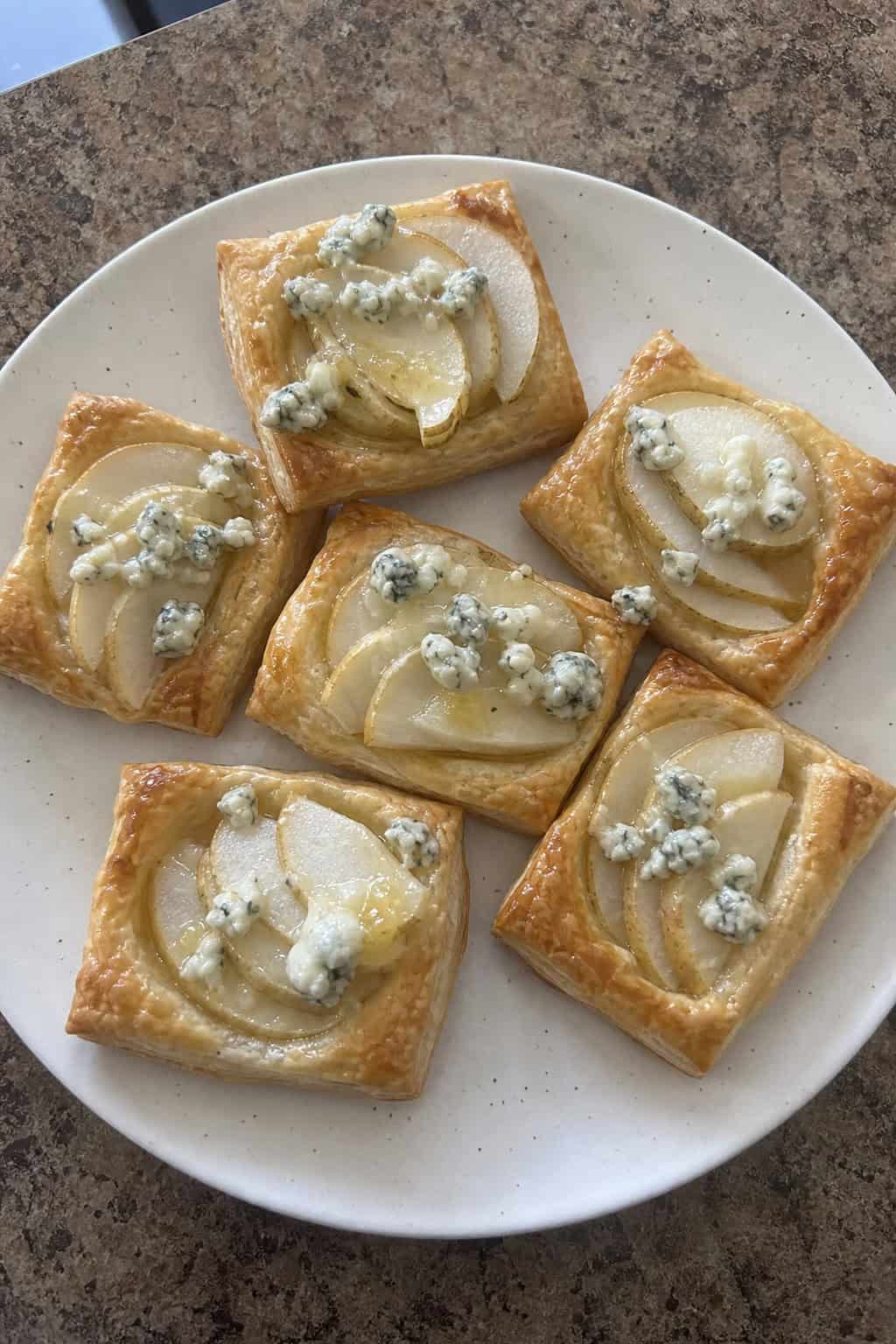 Close-up of pear and gorgonzola puff pastry crostini on a wooden board with fresh herbs.