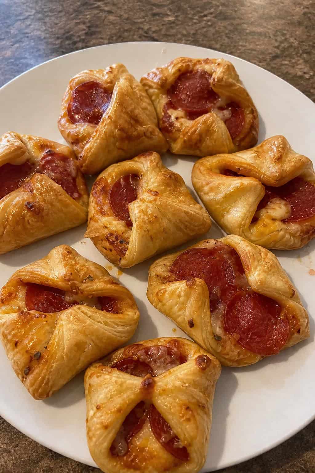 Close-up of golden-brown pepperoni pizza puff pastry purses arranged on a wooden board with herbs in the background.