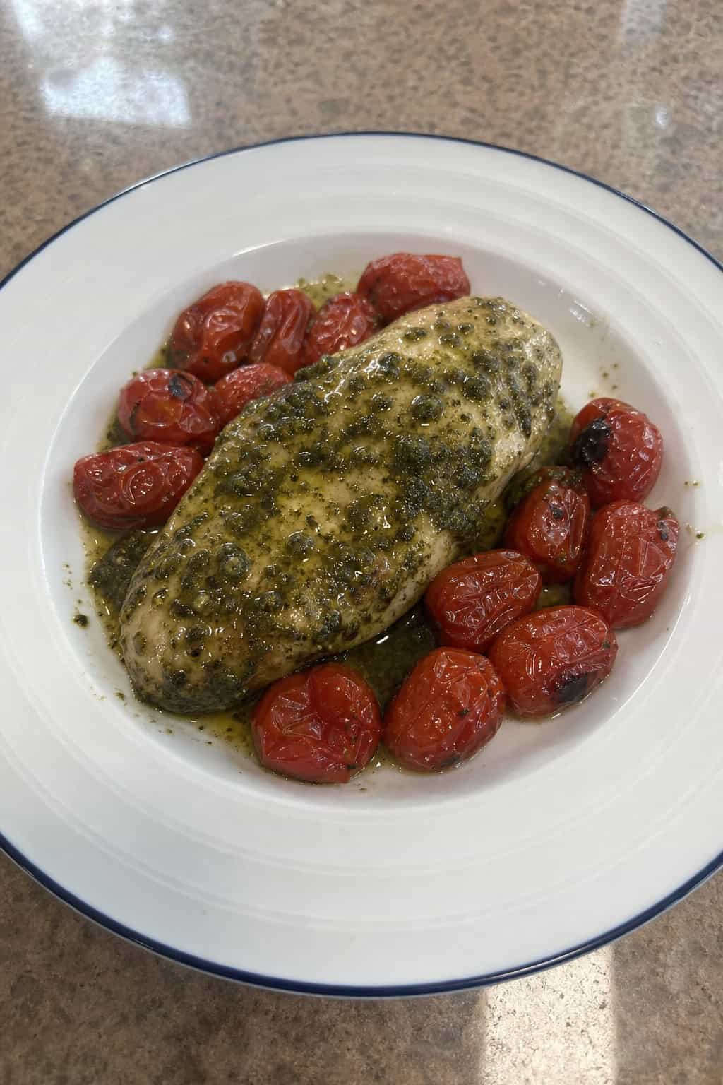 A plate with pesto chicken and roasted cherry tomatoes on a wooden table.