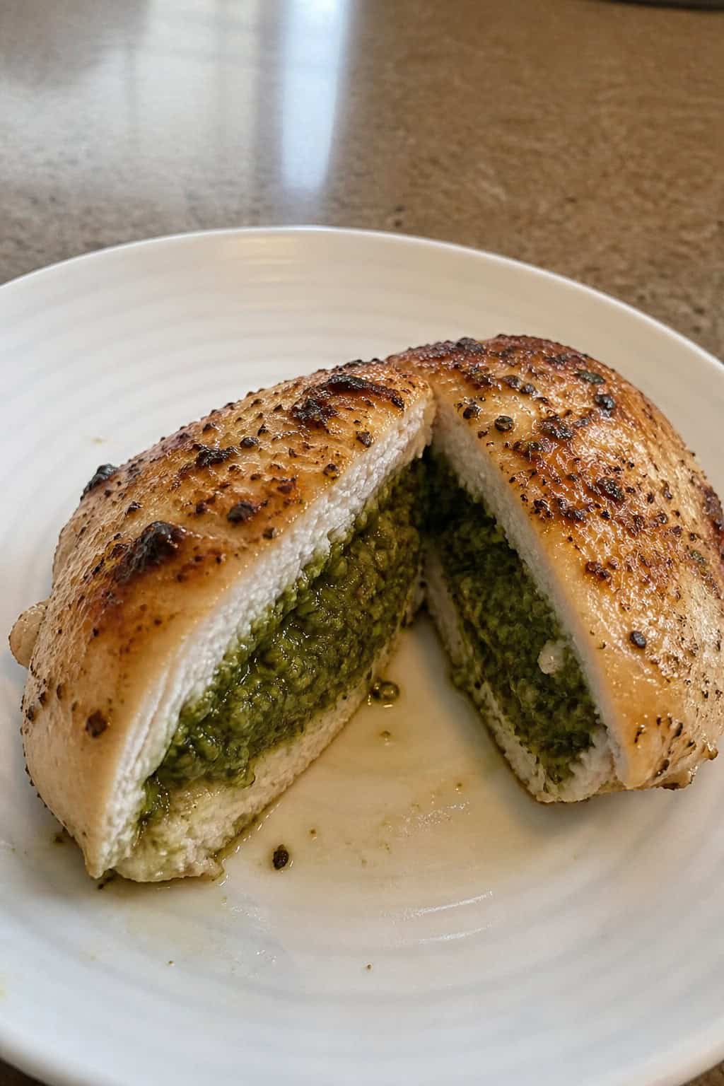A sliced chicken breast stuffed with green pesto on a white plate, garnished with basil leaves and cherry tomatoes.