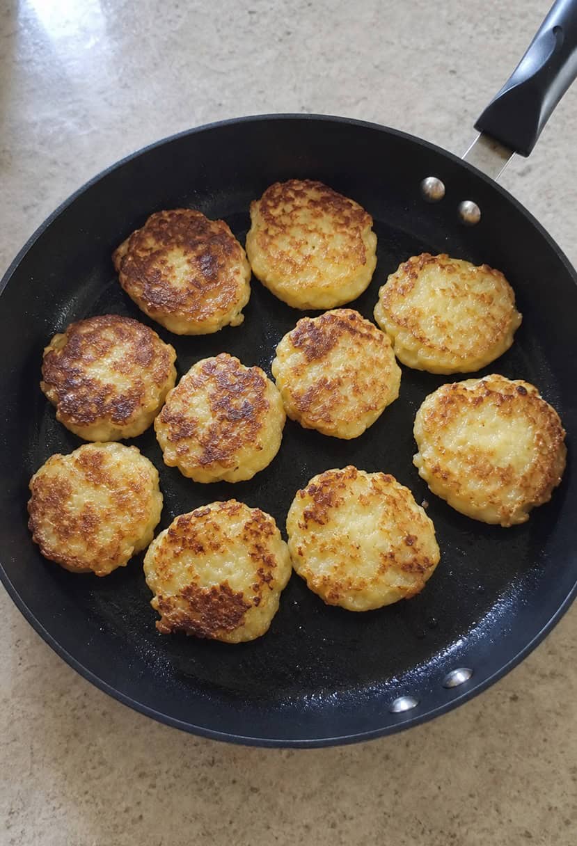 A sizzling skillet of golden-brown potato latkes surrounded by a variety of fresh ingredients and cooking utensils