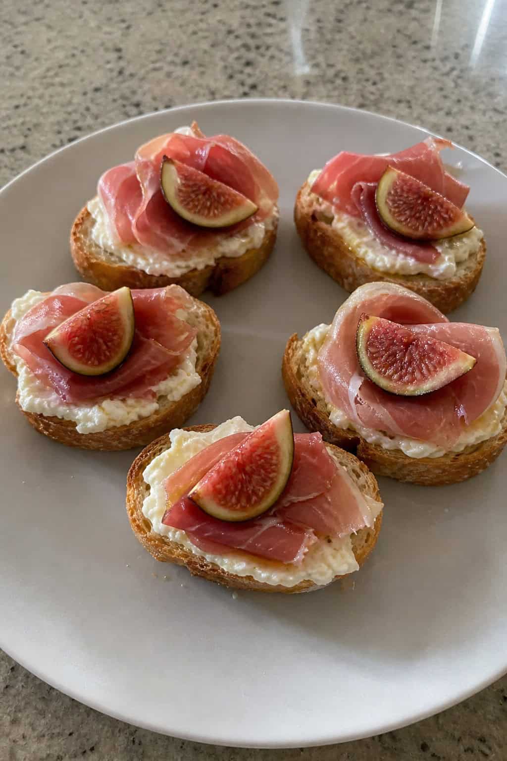 Close-up of prosciutto and fig crostini topped with mascarpone on a wooden serving board.